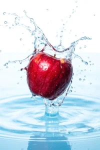 A photorealistic red apple mid-splash in clear water, with frozen droplets and ripples under bright dynamic lighting.